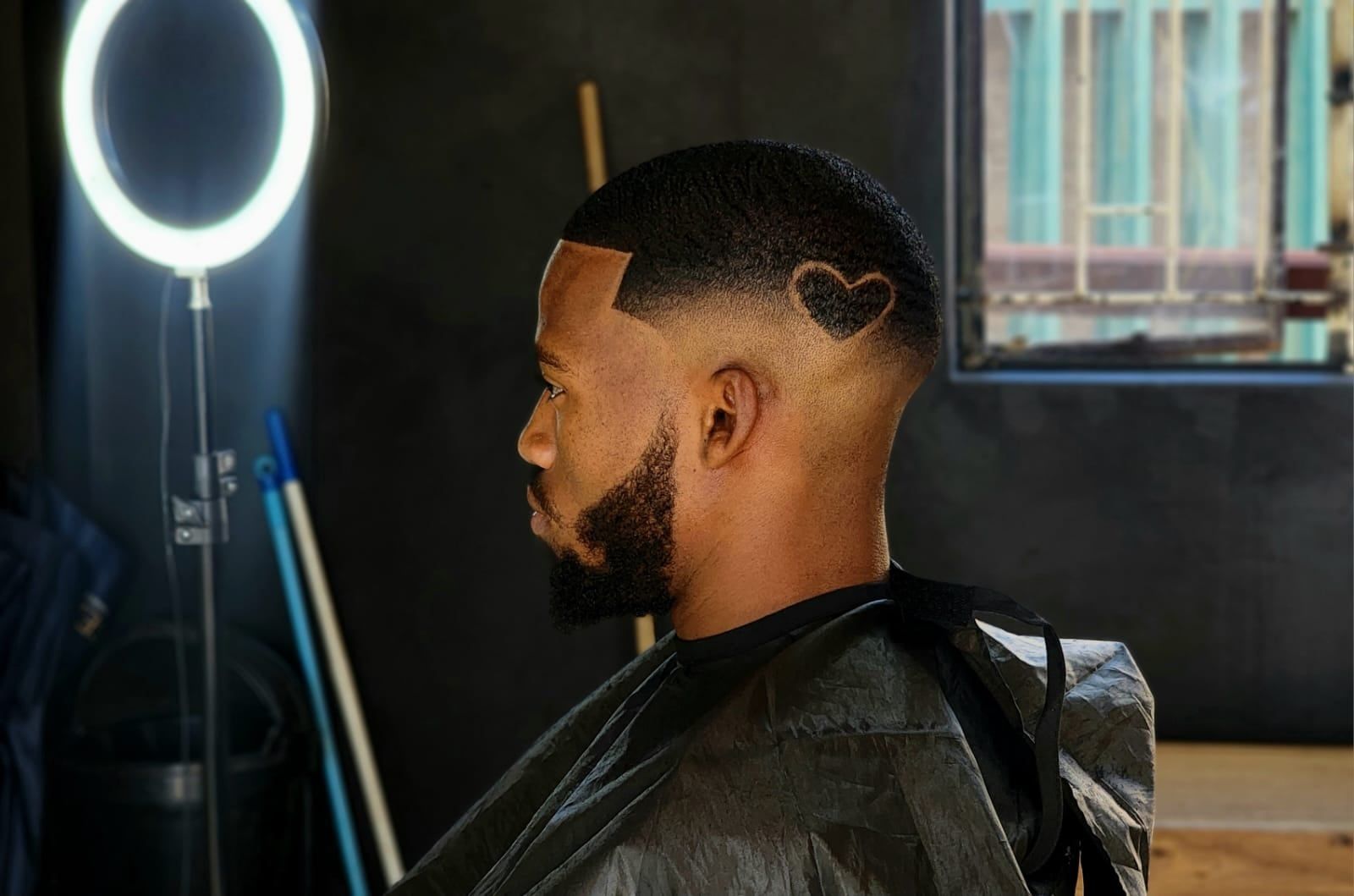 Perfil de un cliente con fade medio, barba perfilada y un diseño de corazón rapado