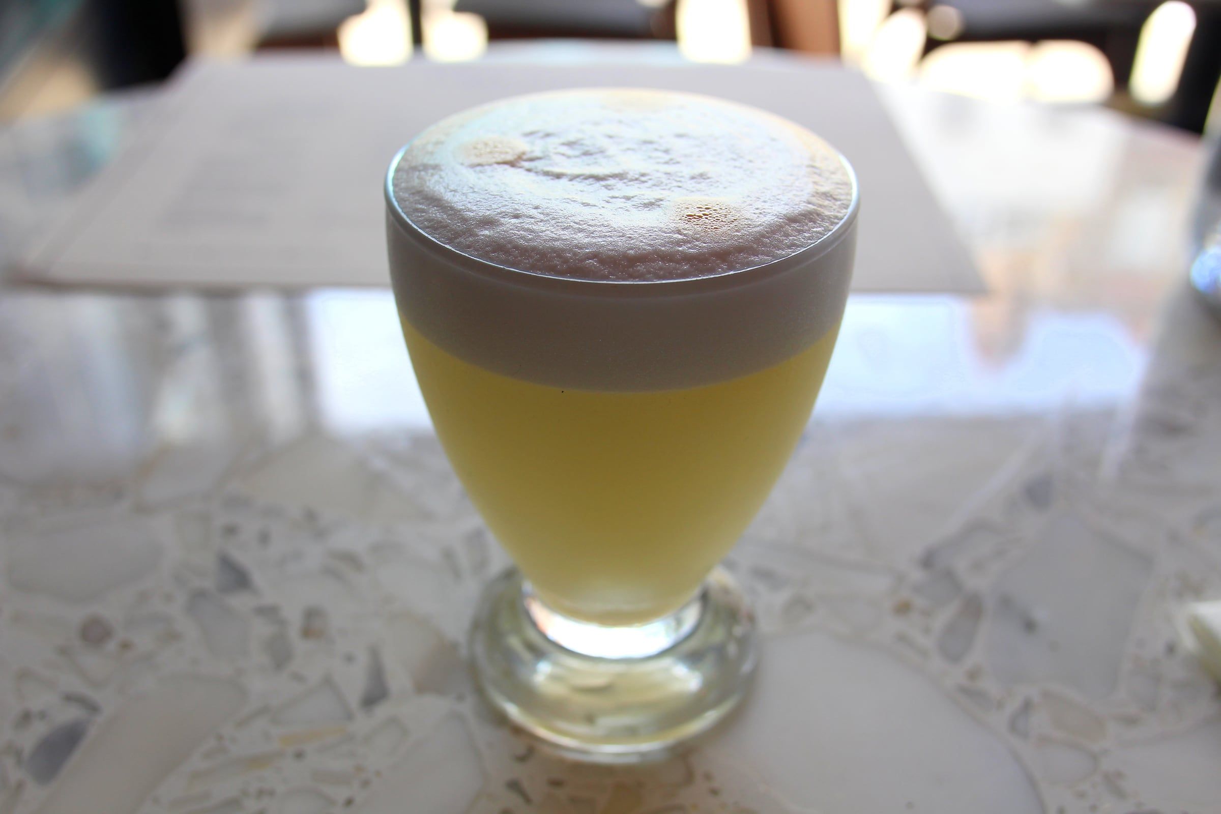 Copa de pisco sour con espuma sobre una mesa clara